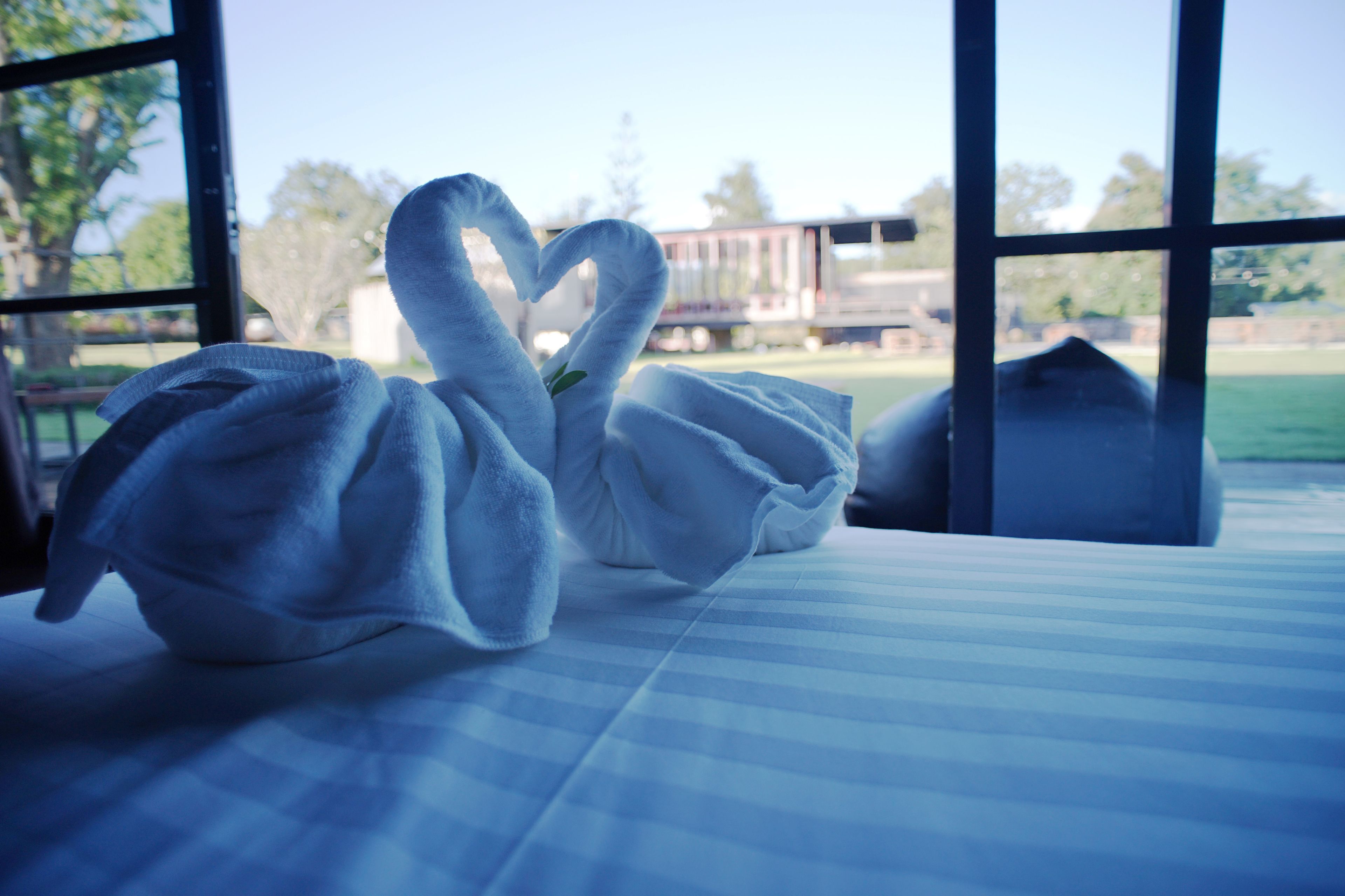 A bed with a blue and white striped bedspread and two swan-shaped towels on it.