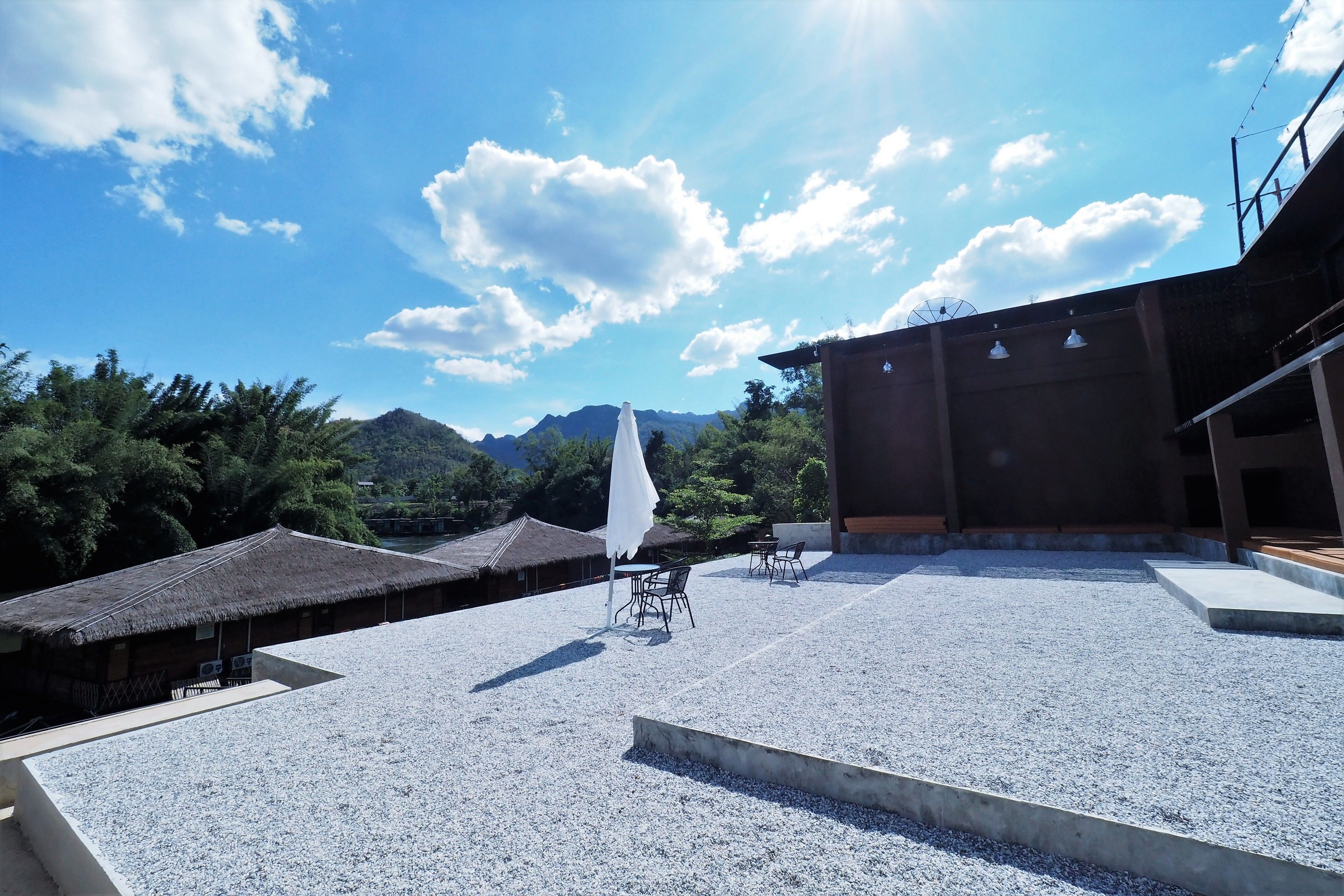 A rooftop terrace with tables and chairs, a white umbrella, and a view of mountains.