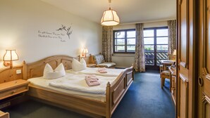 A hotel room with a wooden bed, two bedside tables, a nightstand, a desk, a chair, a window with curtains, and a view of the outdoors. - Berggasthof & Hotel Hinterrod (Eisfeld)