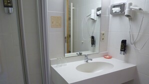 A bathroom with a white sink, a mirror, a hairdryer, and a trash can. - Berggasthof & Hotel Hinterrod (Eisfeld)