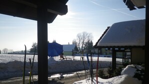 A snowy outdoor area with a covered seating area, a building with a snow-covered roof, and skis leaning against a pole. - Berggasthof & Hotel Hinterrod (Eisfeld)