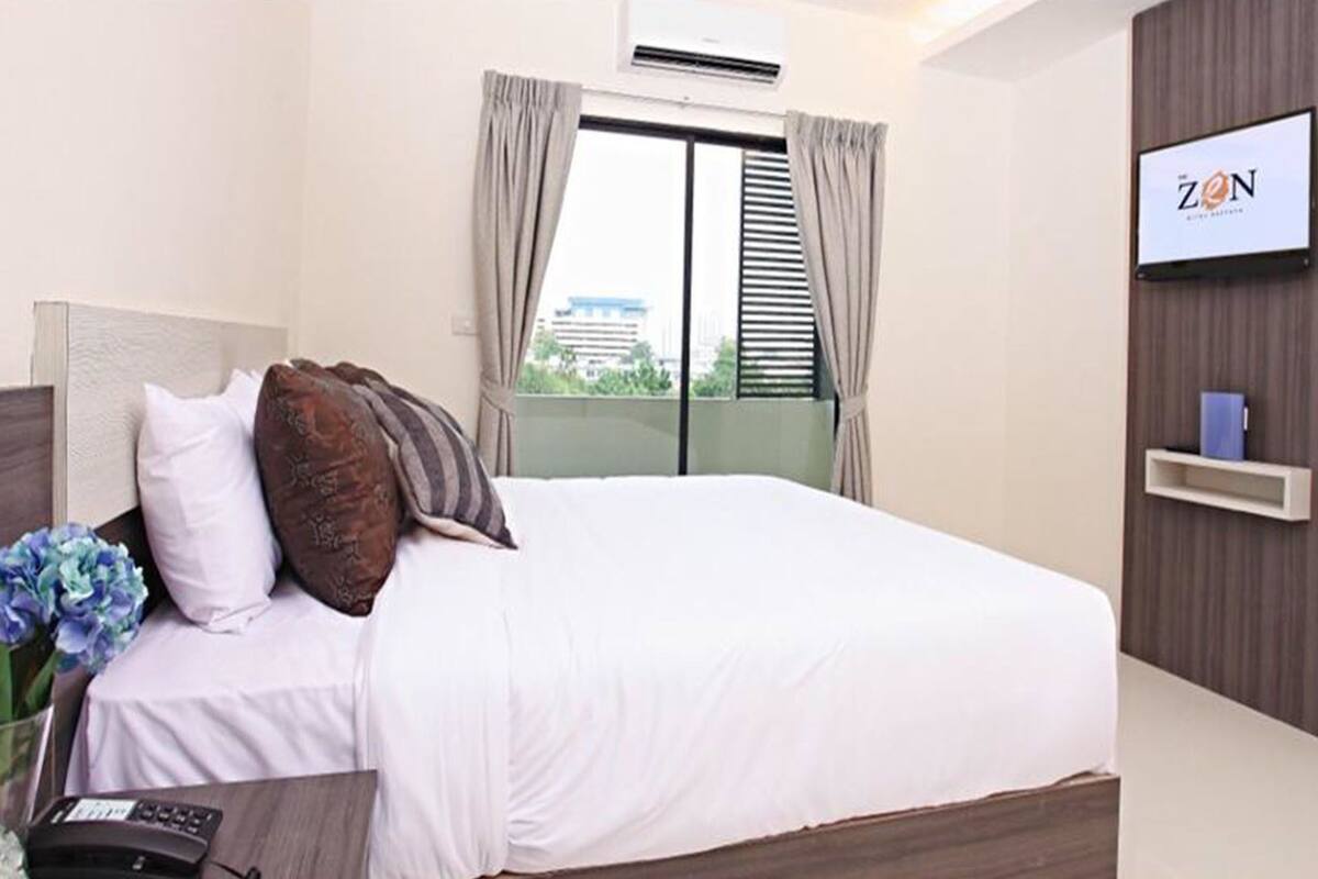 Une chambre d’hôtel avec un lit, un téléviseur fixé au mur et une fenêtre avec des rideaux.