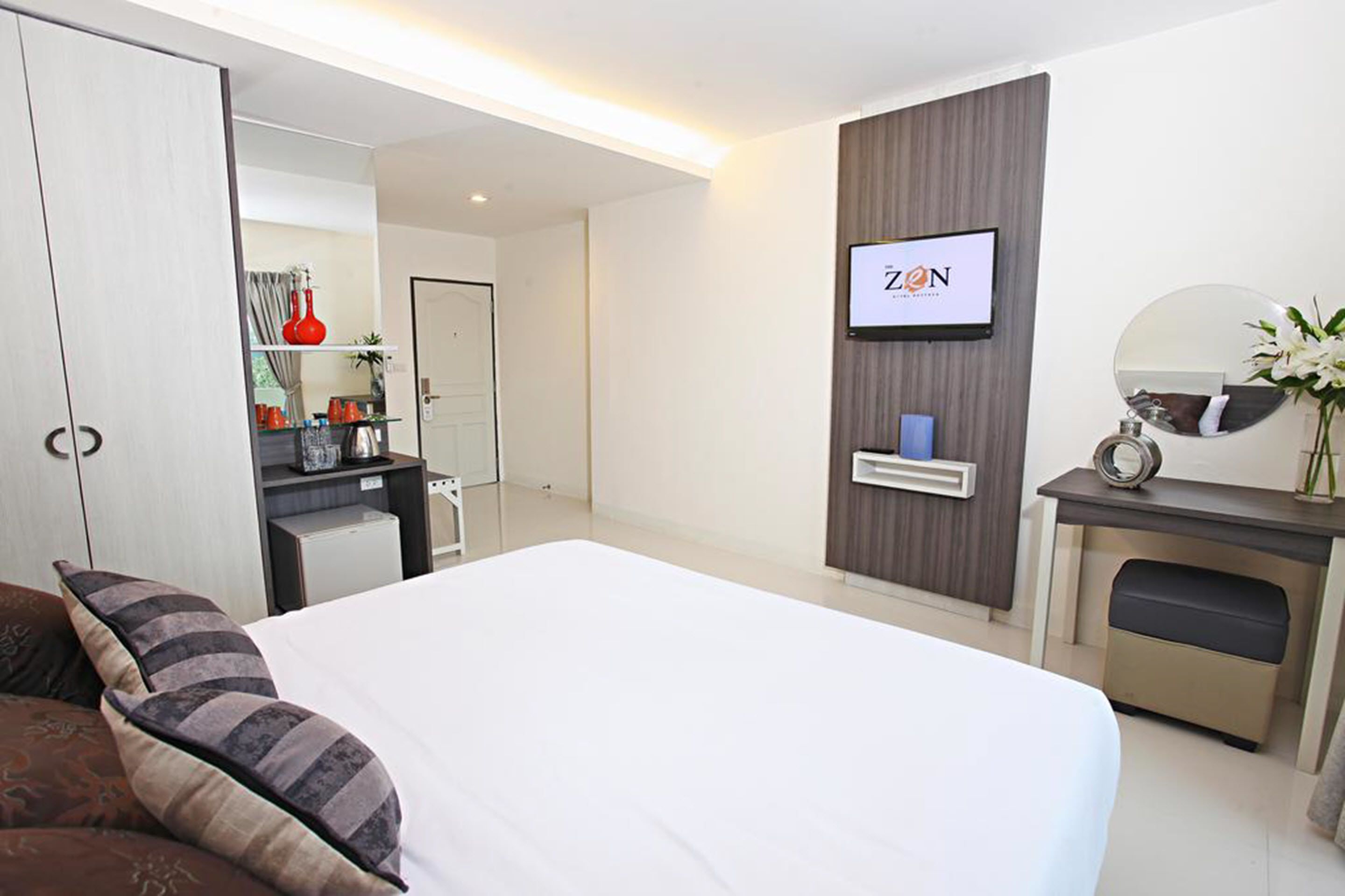 A modern hotel room with a large bed, a desk with a mirror, a wardrobe, and a ZON sign on the wall.