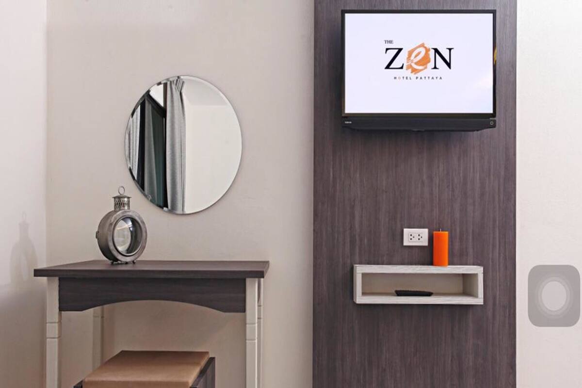 Une chambre d’hôtel moderne avec un miroir rond, une petite table avec une horloge, un téléviseur fixé à un mur en bois et une étagère avec une bougie.
