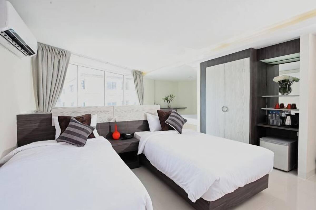 Une chambre d’hôtel moderne avec deux lits, une armoire, un bureau et une grande fenêtre.