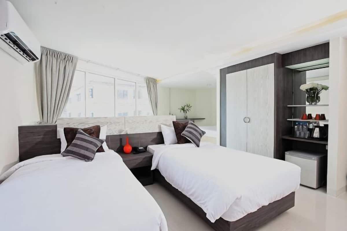 A modern hotel room with two beds, a wardrobe, a desk, and a large window.