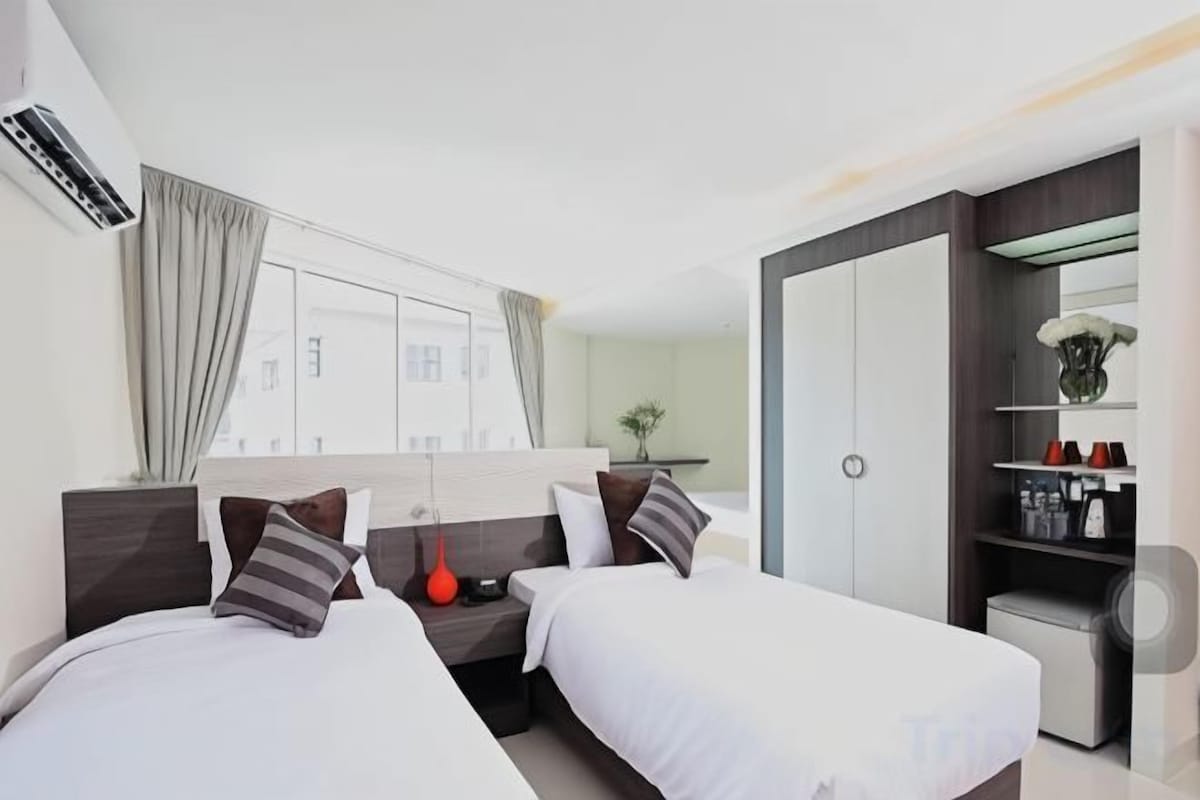 A modern hotel room with two beds, a desk, a wardrobe, and a large window.