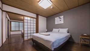 Et moderne hotelværelse med trægulv, en stor seng med hvide sengetøj, en shoji skydedør og et billede hængende på væggen.
