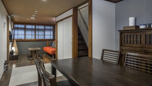 Et værelse med et træbord, stole, en sofa, en trappe og udsigt gennem store vinduer.