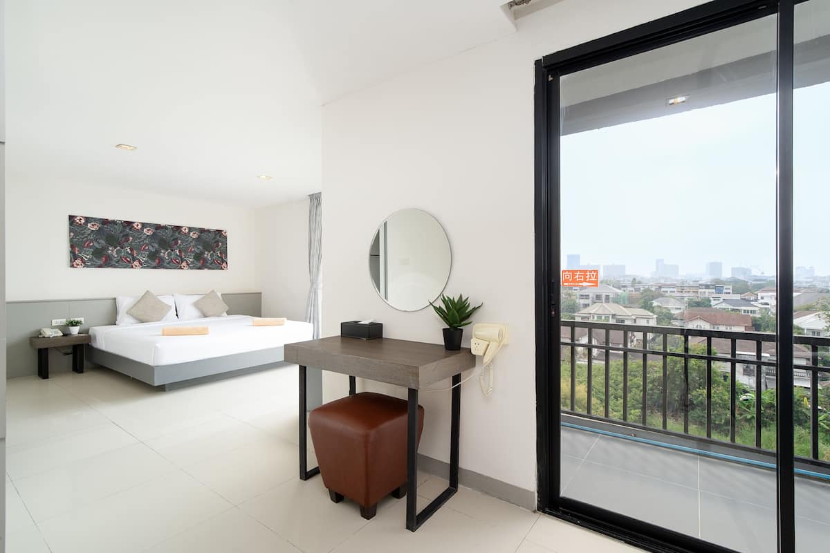A modern hotel room with a bed, a desk, a mirror, a telephone, and a balcony with a city view.