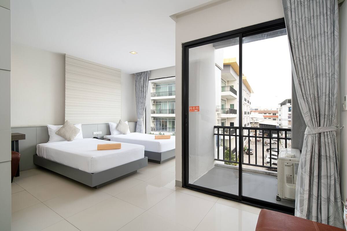 A modern hotel room with two beds, a balcony with a view of the city, and a sliding glass door.