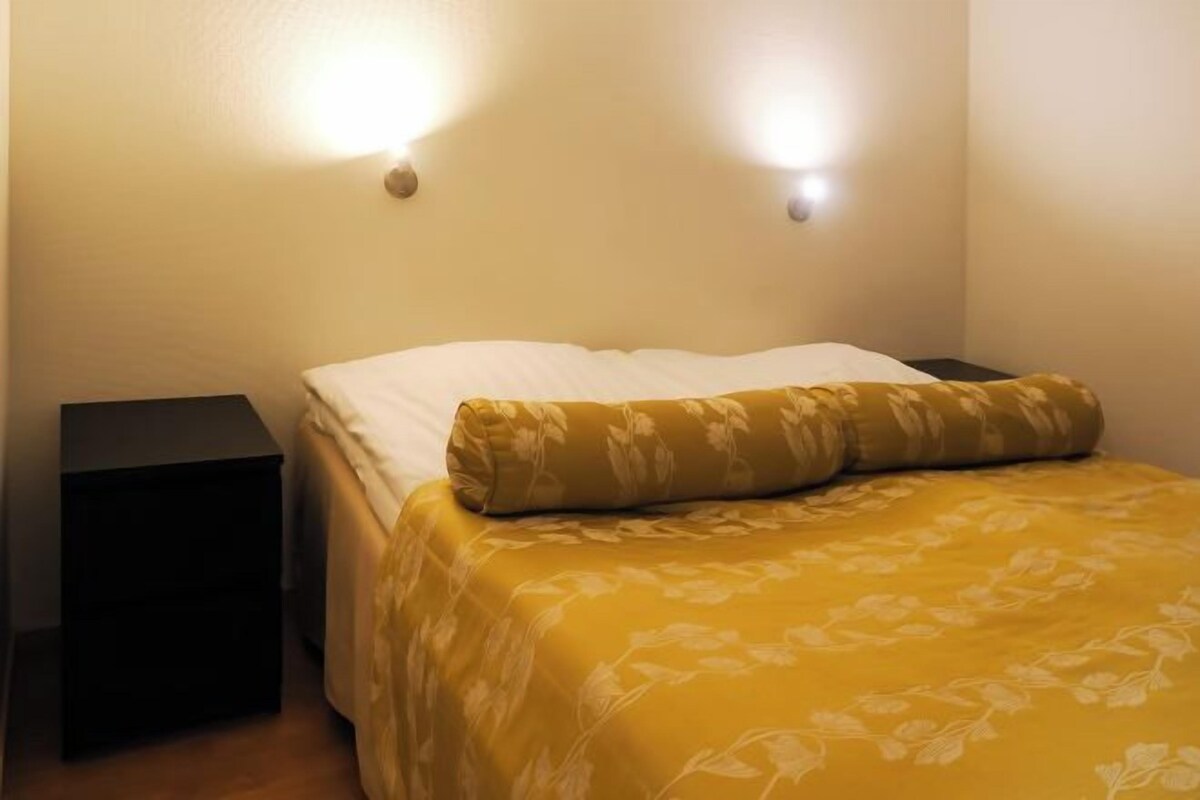 Un dormitorio con una cama, dos mesitas de noche y luces fijadas en la pared.