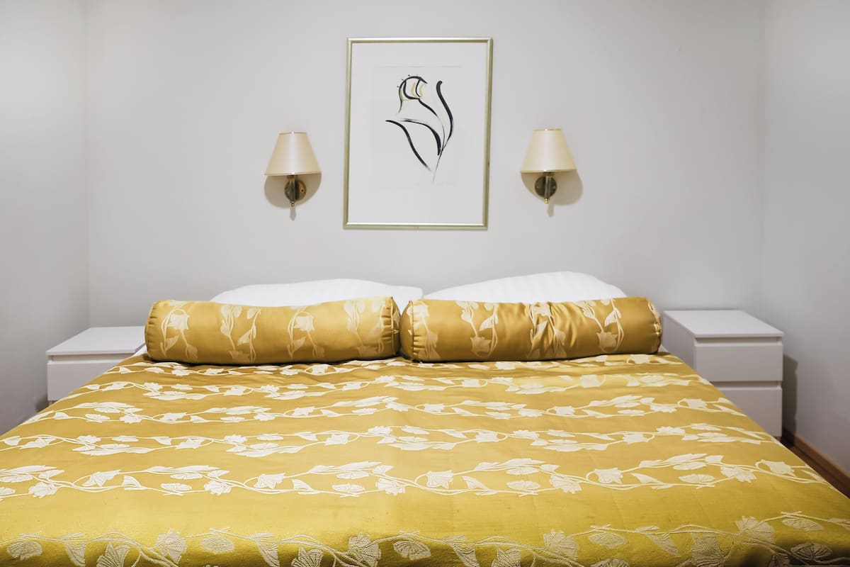 A neatly made bed with a yellow floral bedspread, two matching pillows, and a framed artwork above.