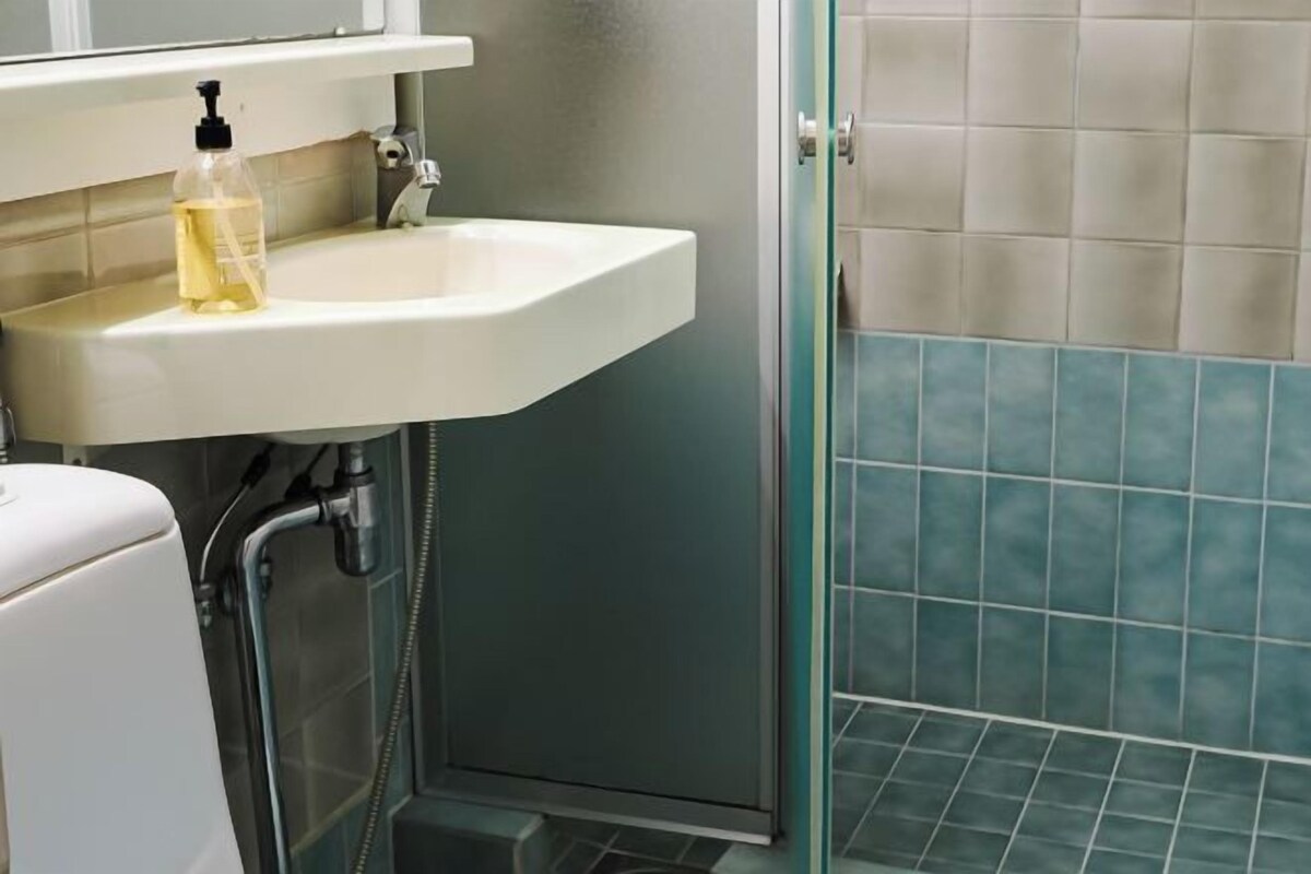A bathroom with a white sink, a bottle of liquid soap, and a shower area with blue tiles.