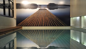 Una larga terraza de madera que se extiende hacia un lago tranquilo, reflejando el cielo y los árboles.