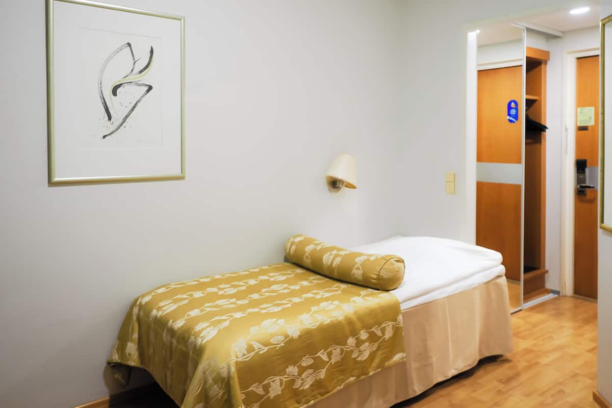A small, neatly arranged bedroom with a bed, a bedside lamp, and a framed artwork on the wall.