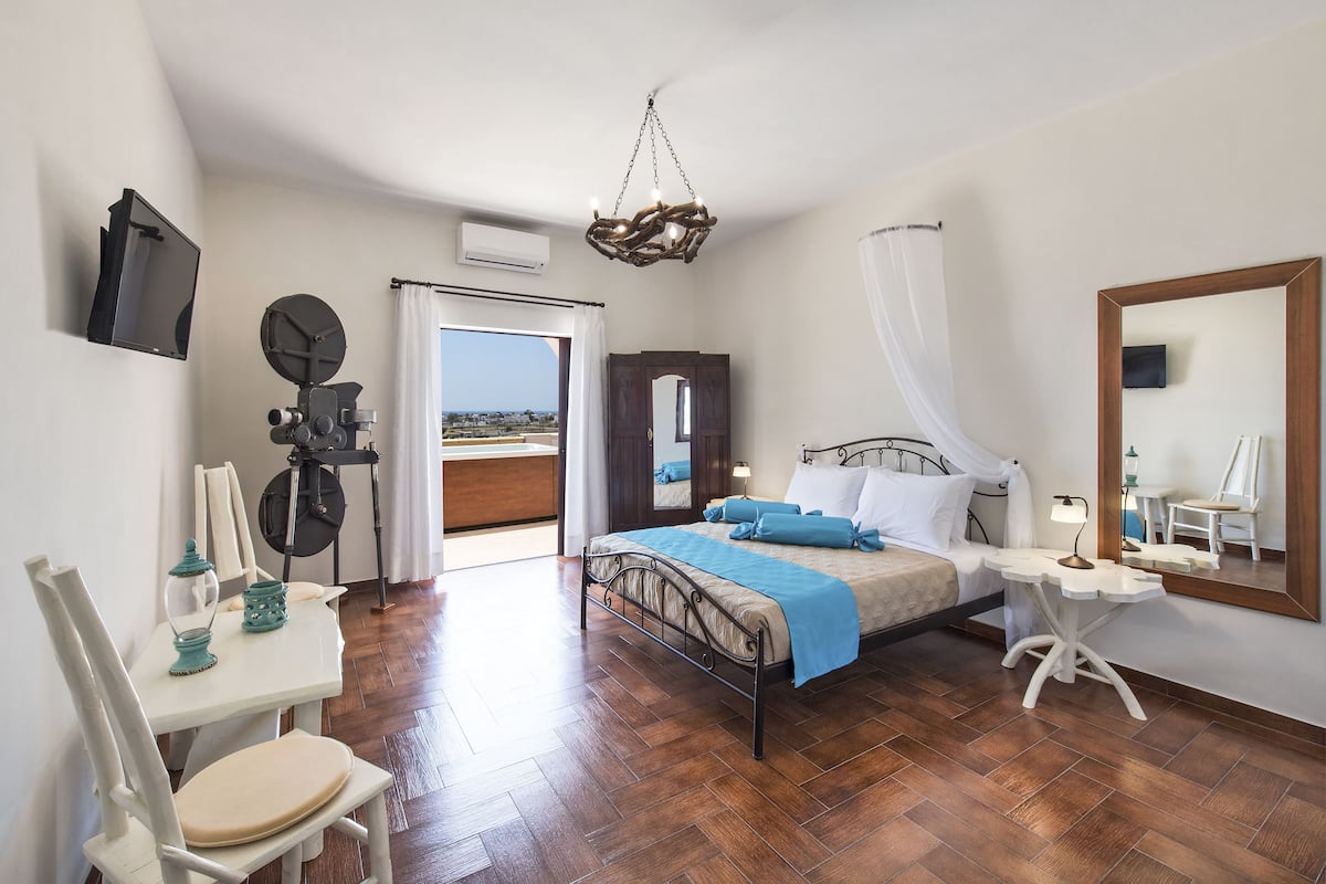 A bedroom with a bed, a desk, a chair, a television, and a large mirror.