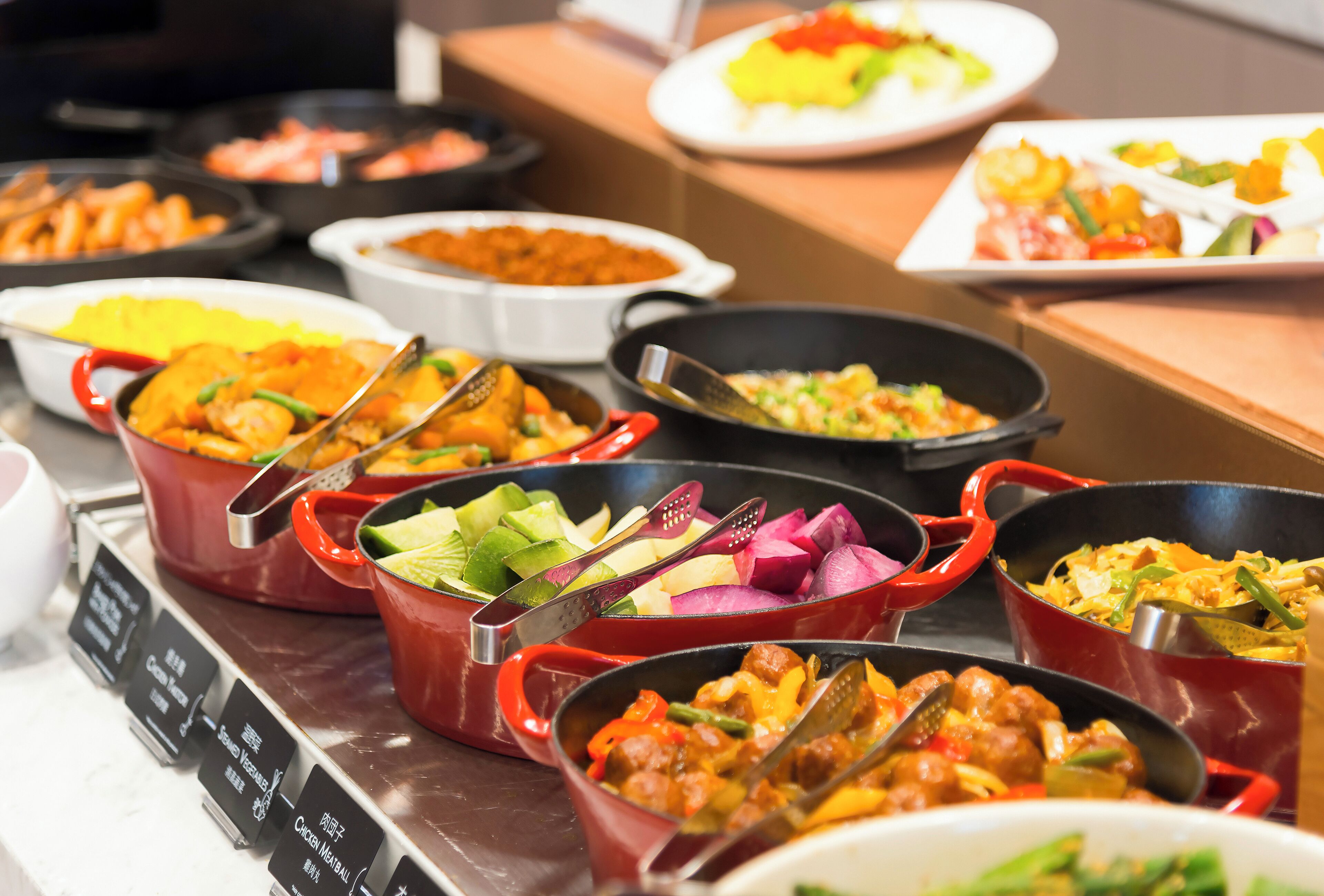 A buffet with various dishes in red and black pots, including vegetables and meats.