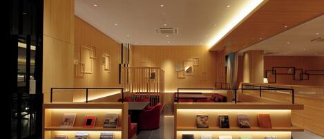 Un moderno hall de hotel con paneles de madera, un mostrador de recepción y zonas de estar con estanterías.