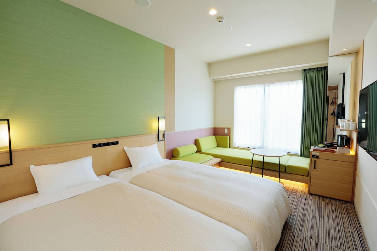 A hotel room with two beds, a sofa, a small table, a TV, and a minibar.