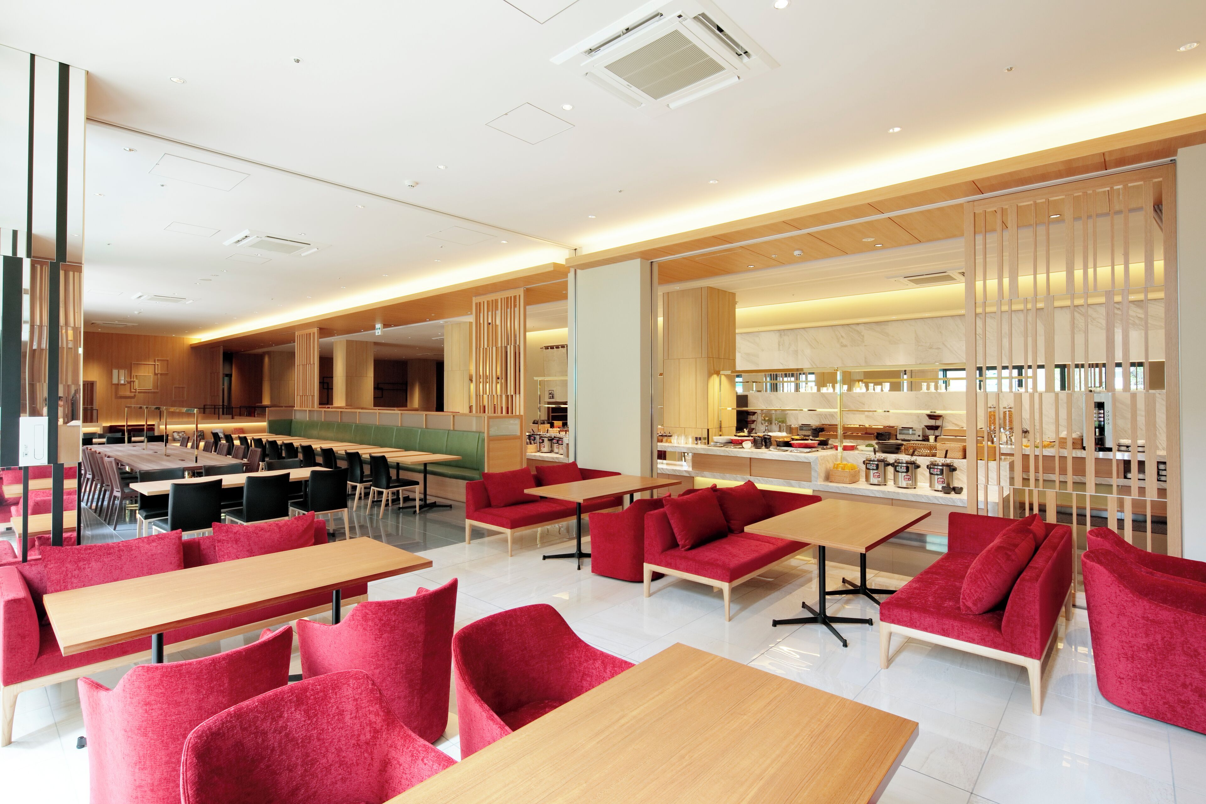 A modern restaurant with red seating, wooden tables, and a kitchen area in the background.
