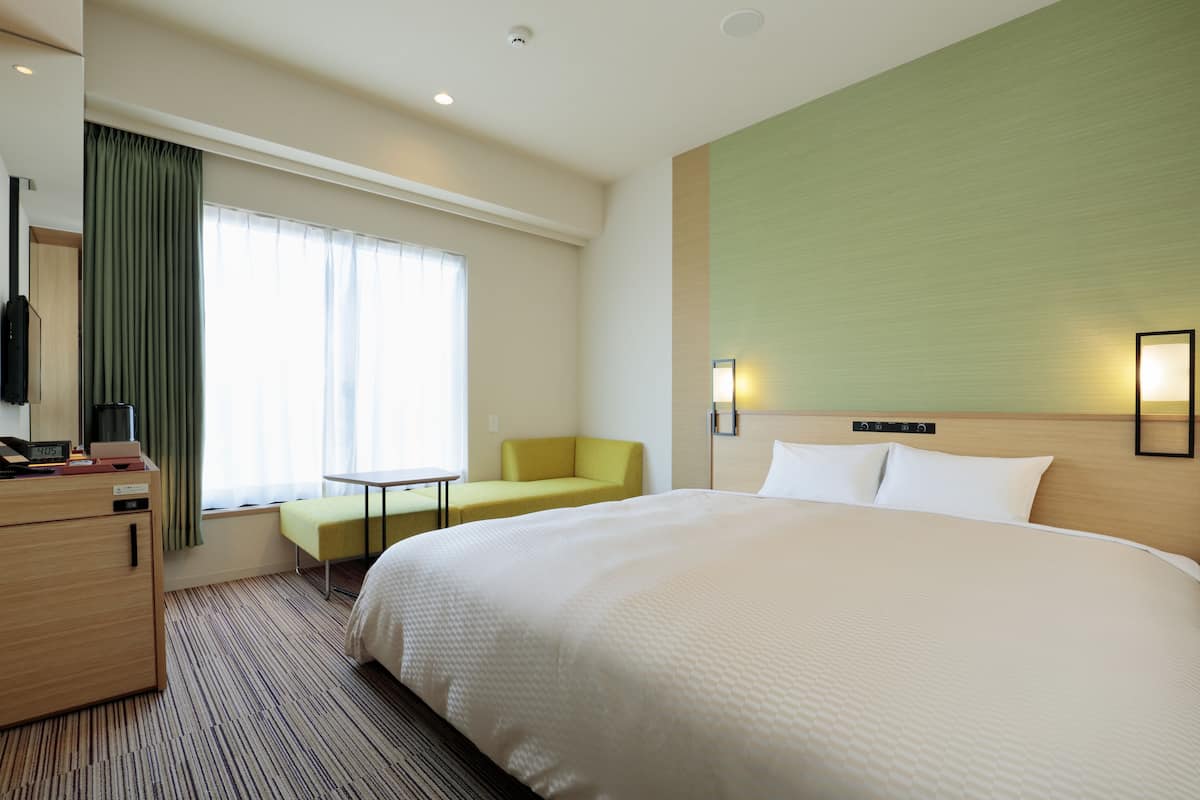 A hotel room with a large bed, a desk, a chair, a television, and a window with curtains.
