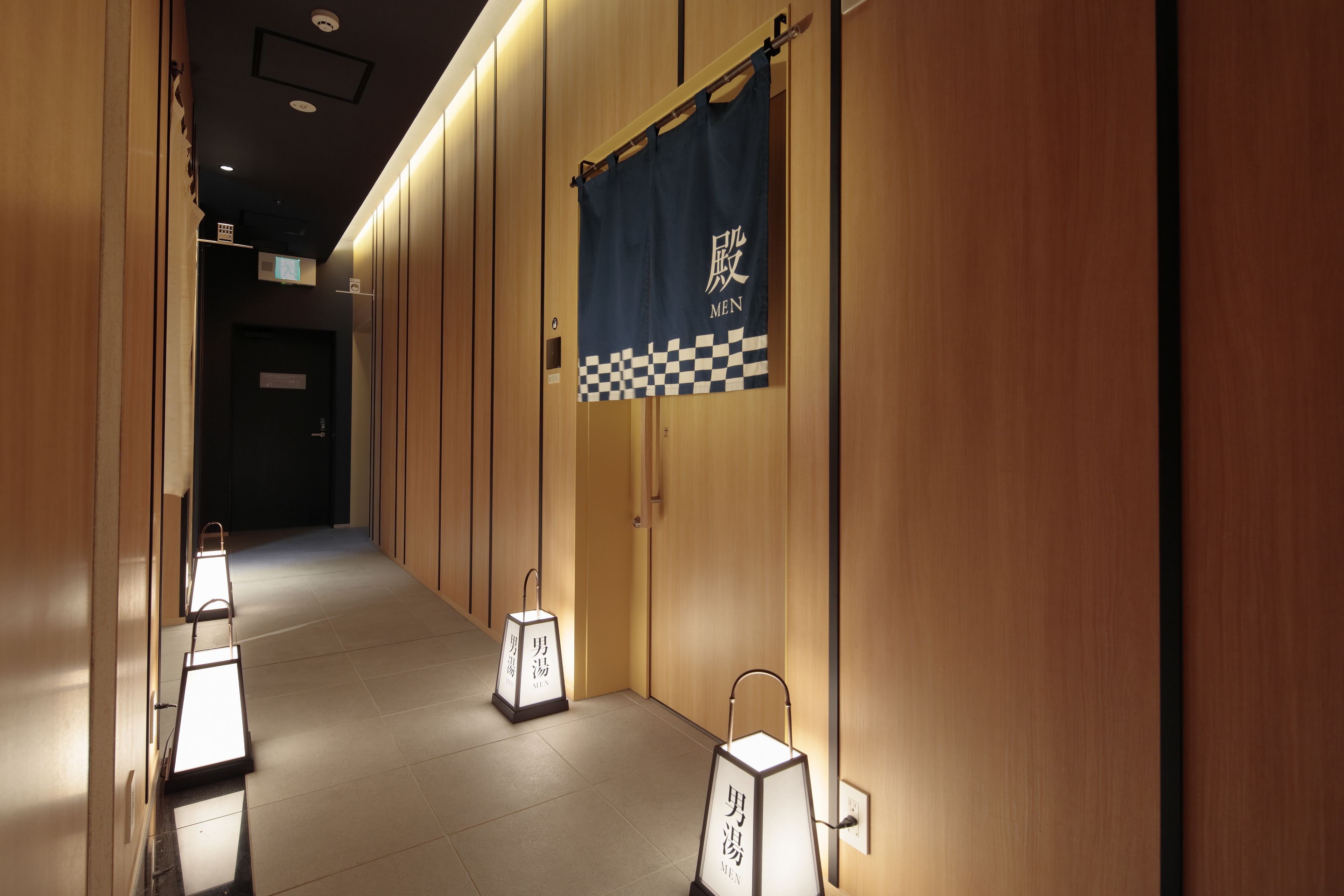 Un pasillo con paneles de madera, un banderín azul con el texto 'MEN' y letreros iluminados con el texto 'MEN'.