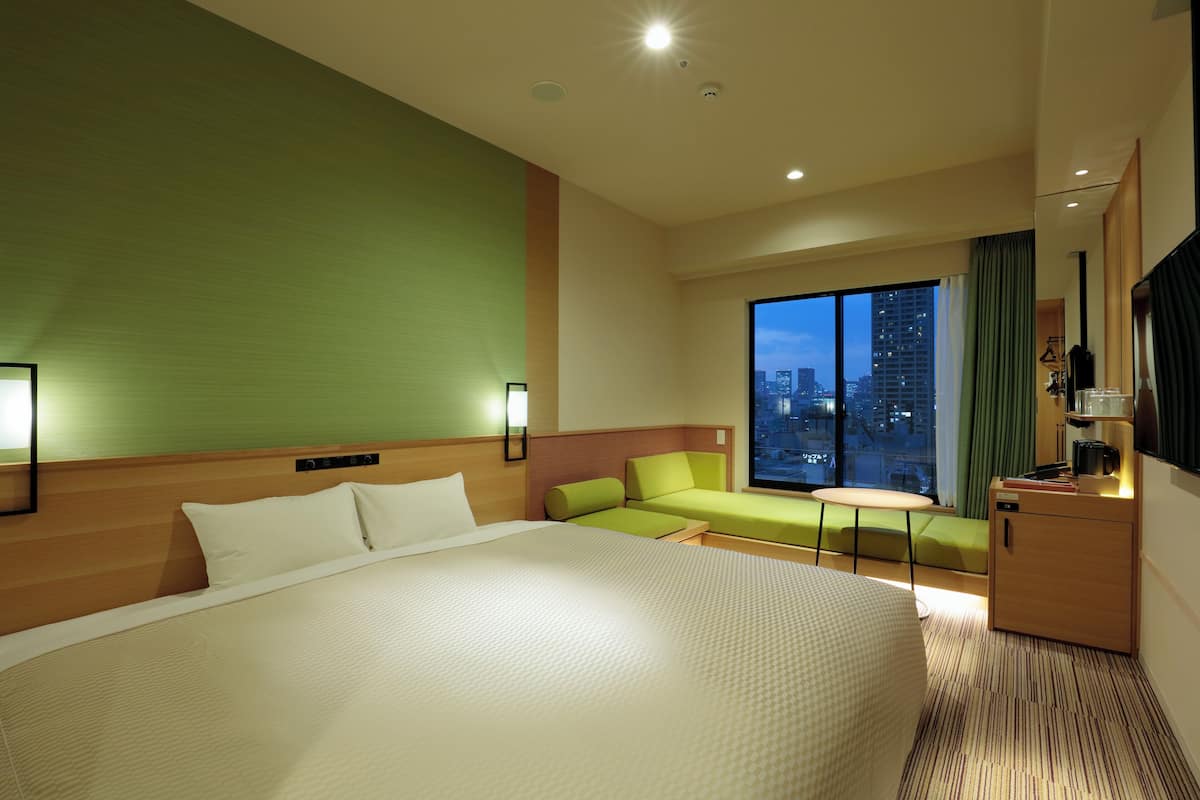 A hotel room with a large bed, a green wall, a seating area, and a view of the city at night.