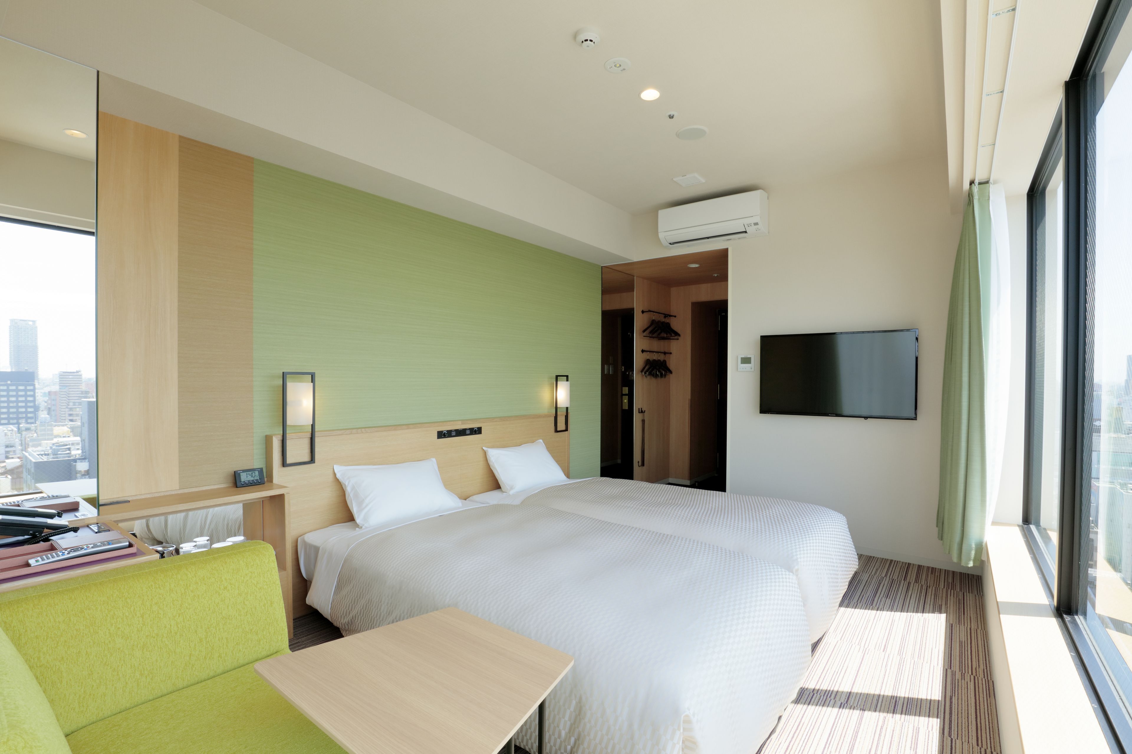 Une chambre d’hôtel avec un grand lit, un bureau, un fauteuil vert et un téléviseur fixé au mur.