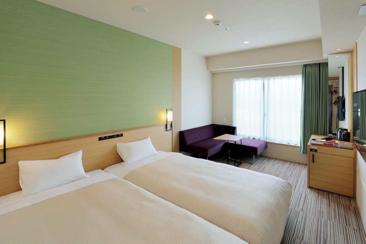 A hotel room with two beds, a desk, a chair, and a small table.