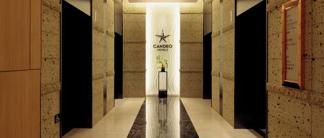 Un moderno vestíbulo de hotel con piso de mármol pulido, un mostrador de recepción central y un letrero de Candeo Hotels.