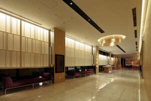 En rymlig entréhall med modern design, med en receptionsdisk, en sittgrupp och en stor kristallkrona.
