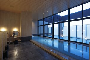 Una piscina interior moderna con amplios ventanales, suelo de baldosas y techo de madera.