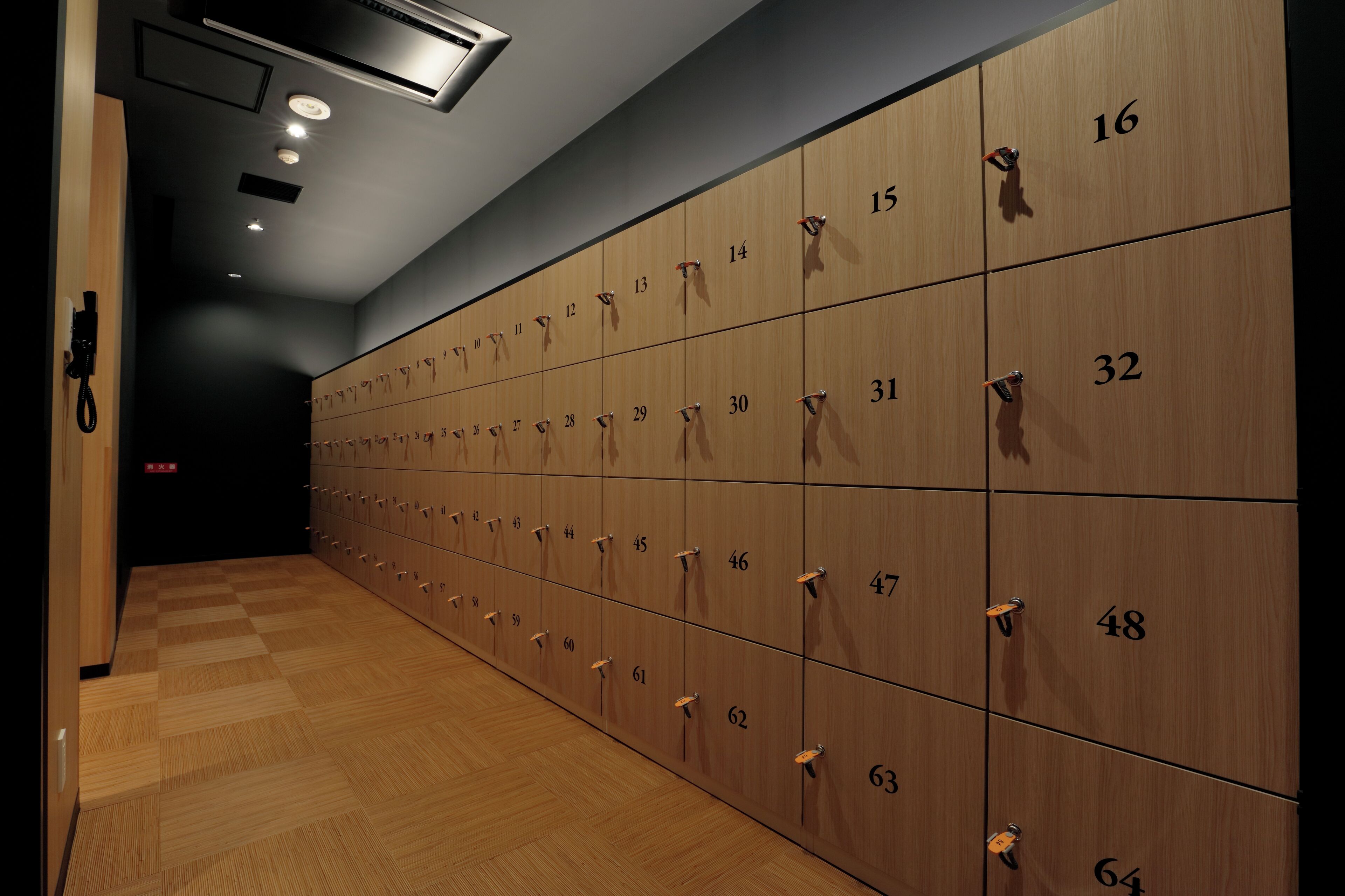 A row of wooden lockers with numbers, a wooden floor, and a ceiling with recessed lighting.