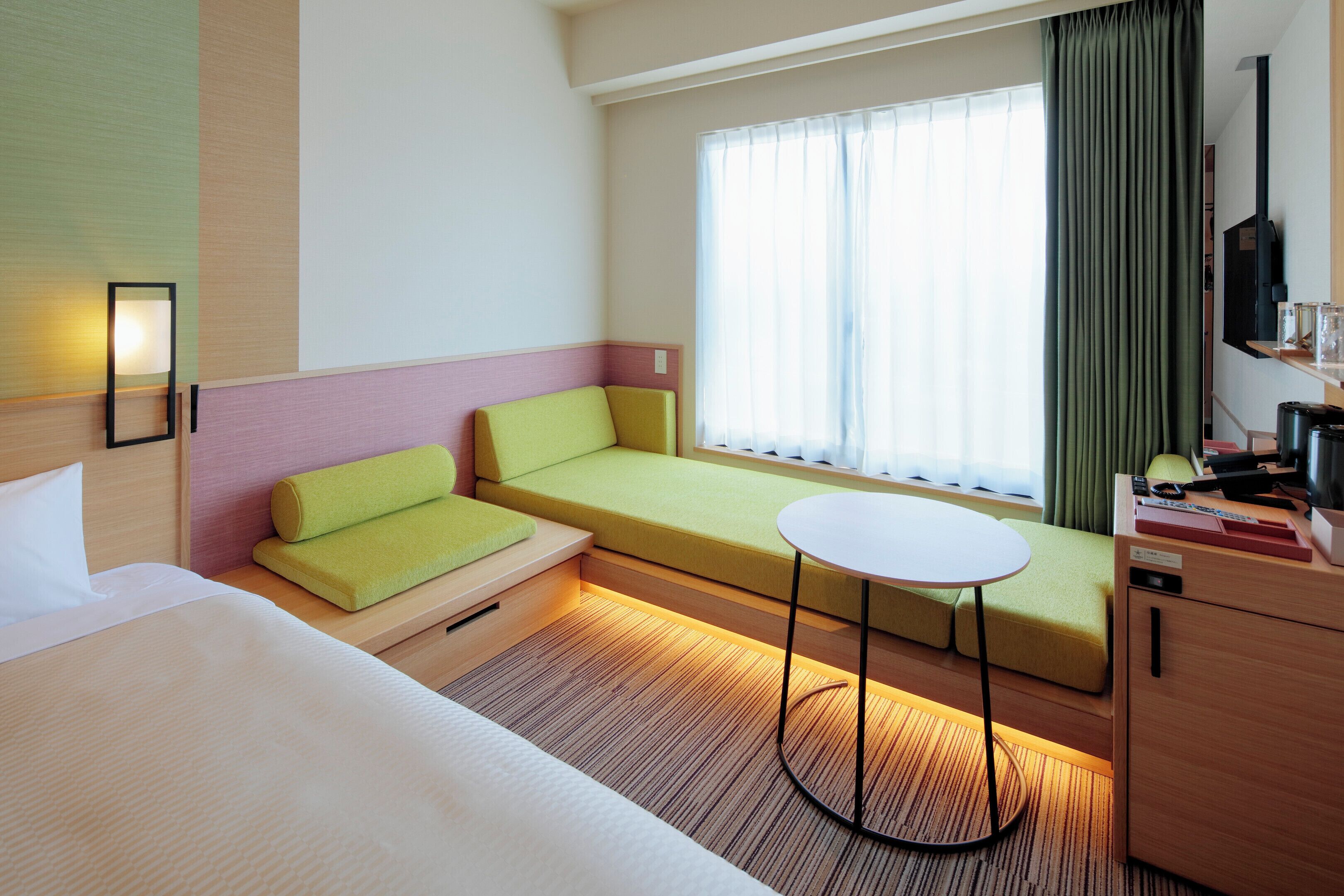 Habitación de hotel con cama, sofá, una mesita, televisor y ventana con cortinas.