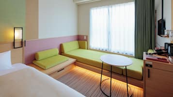 Habitación de hotel con cama, sofá, una mesita, televisor y ventana con cortinas.