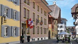 A traditional European street with a hotel featuring a signboard, outdoor seating, and a cobblestone street. - Hotel Engel (Zofingen)