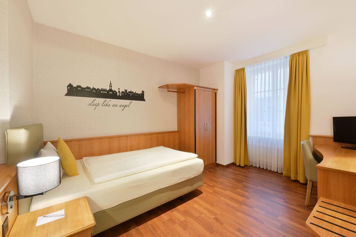 A hotel room with a bed, a desk, a chair, a TV, a wardrobe, and a wall decoration.