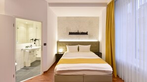 A modern hotel room with a large bed, a nightstand, a wall-mounted cityscape artwork, and a bathroom visible through an open door. - Hotel Engel (Zofingen)