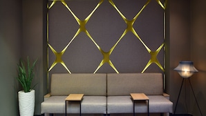 A modern waiting area with a sofa, a potted plant, and a floor lamp. - Hotel Engel (Zofingen)