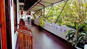 A covered balcony with wooden chairs, potted plants, and a view of trees. - Hotel Happy Night & Restaurant (Unawatuna)