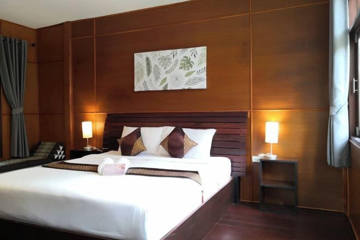 A hotel room with a large bed, wooden panel walls, a wall-mounted artwork, two bedside lamps, and a small table with a lamp.
