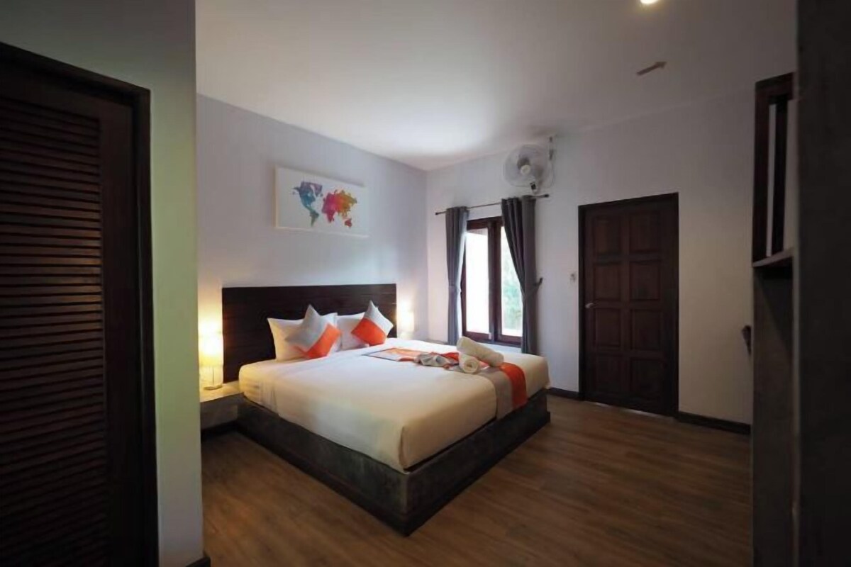 A hotel room with a large bed, a wooden floor, a nightstand, a wall-mounted air conditioner, and a door.