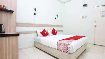 A hotel room with a bed, a wooden headboard, a bedside table, a red and white patterned blanket, and a red pillow.