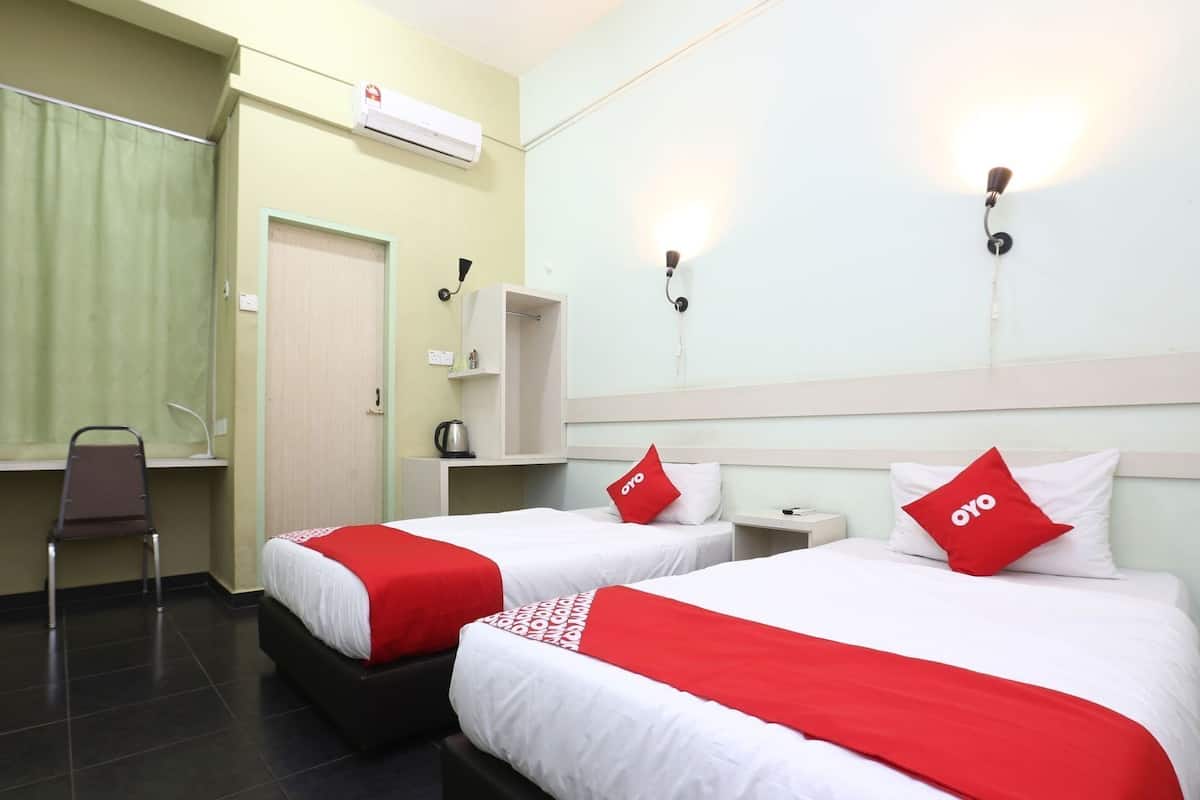 Une chambre d’hôtel avec deux lits, une chaise, une étagère avec une bouilloire et un climatiseur fixé au mur.