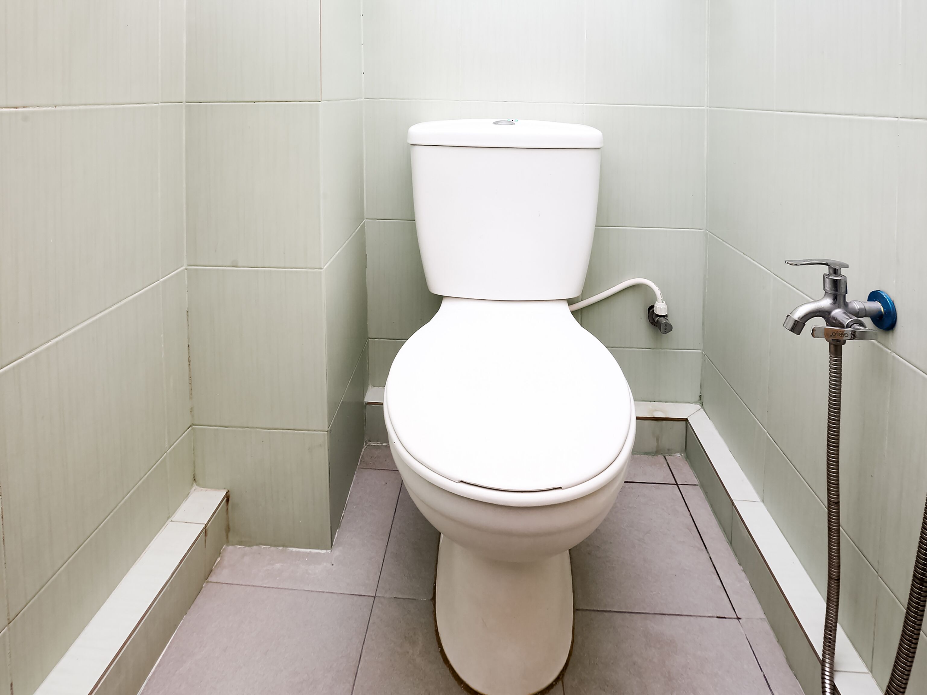 A standard white toilet in a small bathroom with light green walls and a tiled floor.