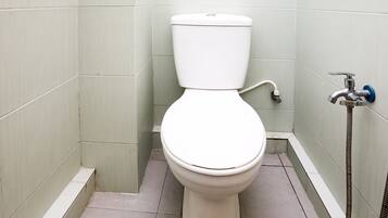 A standard white toilet in a small bathroom with light green walls and a tiled floor.