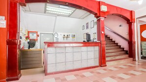 Un espace d’accueil avec une arche rouge, un comptoir d’accueil, une horloge et un escalier menant à l’étage supérieur.