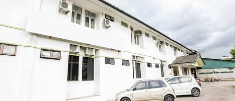 Un edificio blanco con múltiples ventanas y unidades de aire acondicionado, un coche blanco estacionado, y un letrero que dice "GREEN MANGO SRI CEMERLANG".