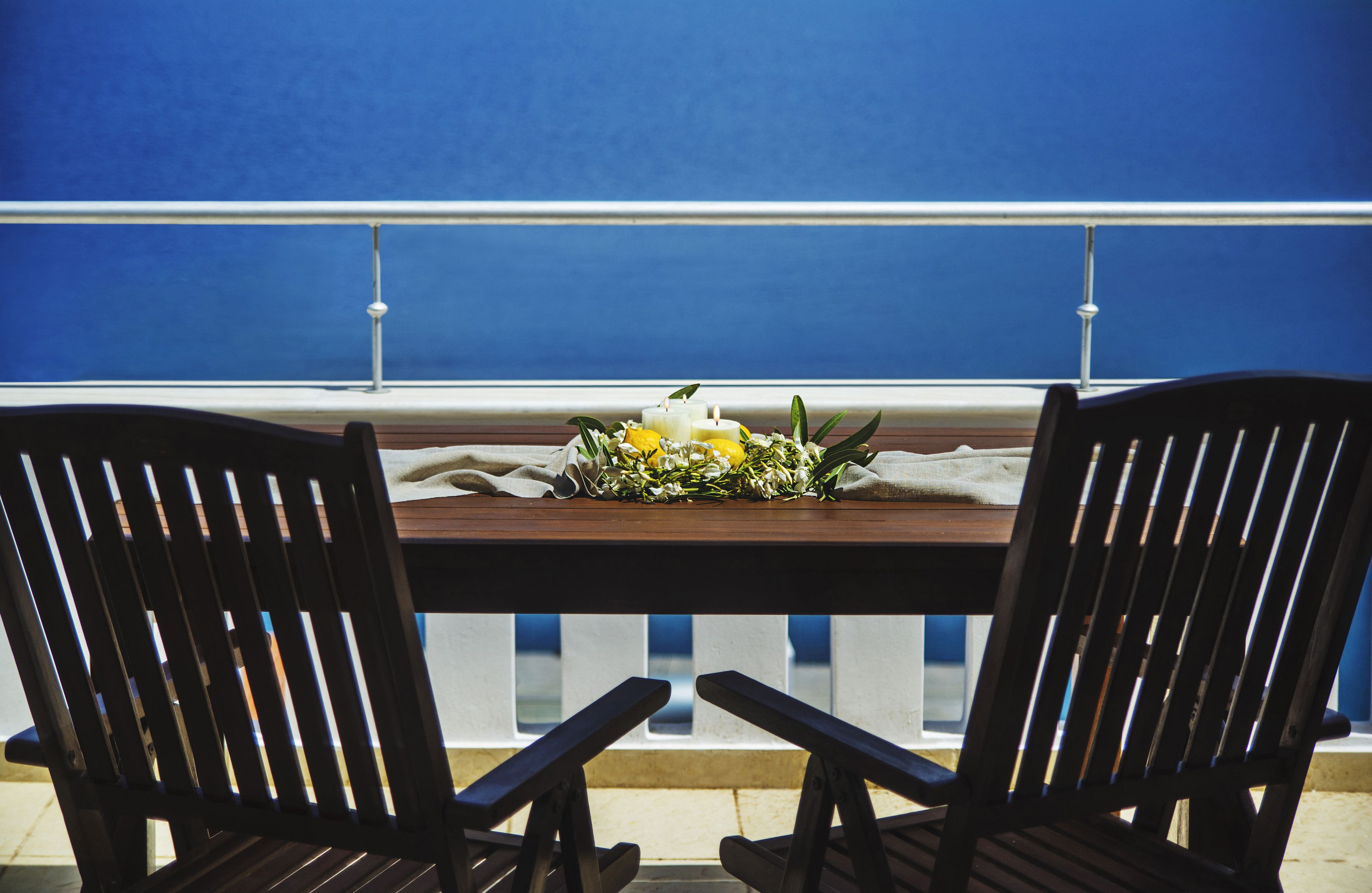 Ein Balkon mit einem Holztisch, gedeckt für zwei Personen, mit floralem Mittelstück und Kerze.